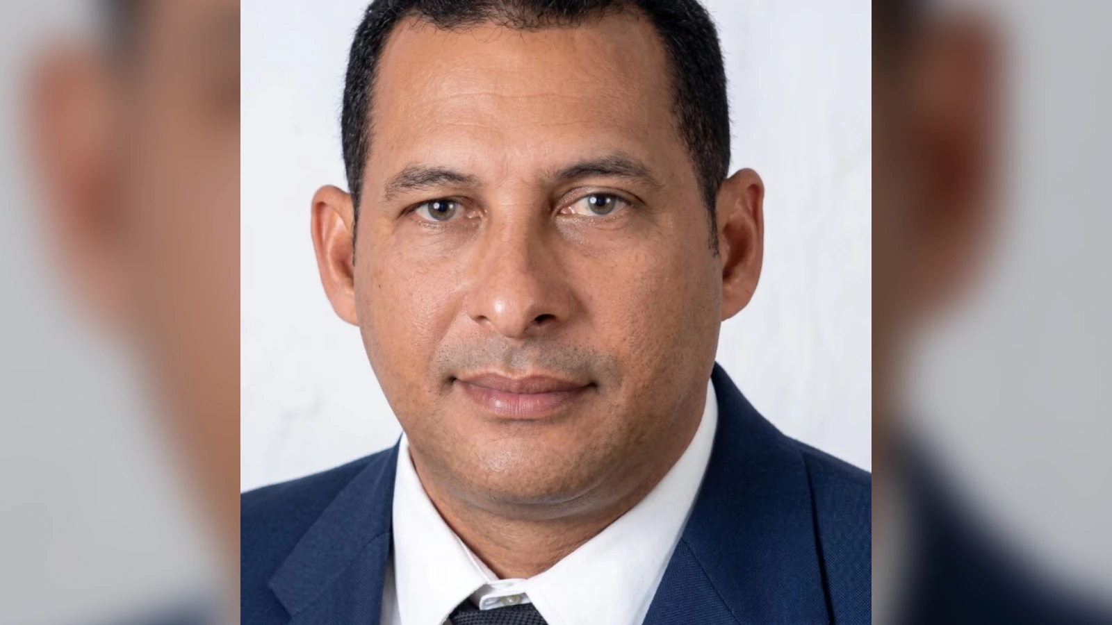 Professional headshot of a man in a navy suit and white shirt, looking at the camera with a neutral expression.