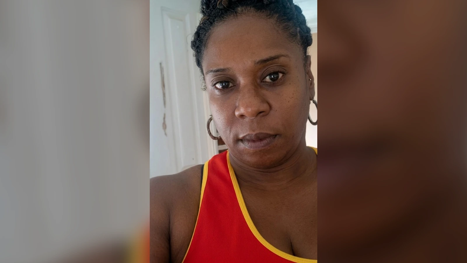 Close-up portrait of a woman with braided hair wearing a red tank top with yellow trim, looking at the camera with a neutral expression.