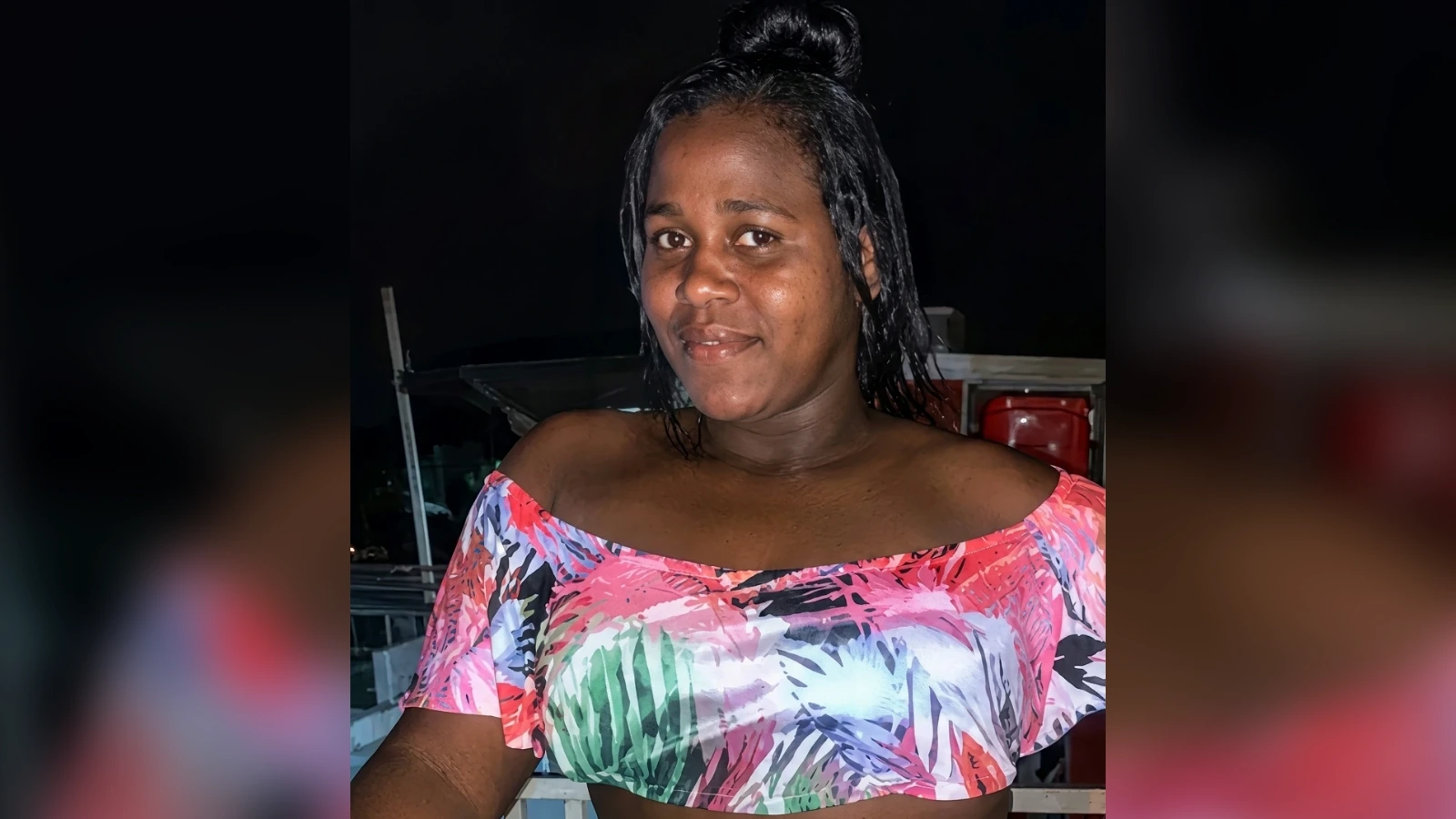 Portrait of a woman wearing a bright, off-the-shoulder floral top at night and smiling.