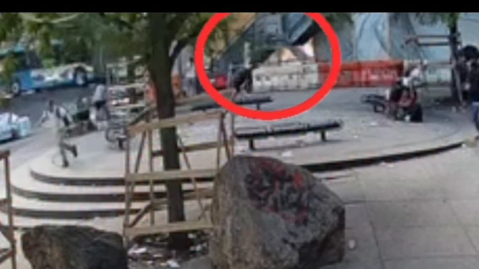Person on the ground beside a bench in a city park, circled in red for emphasis.
