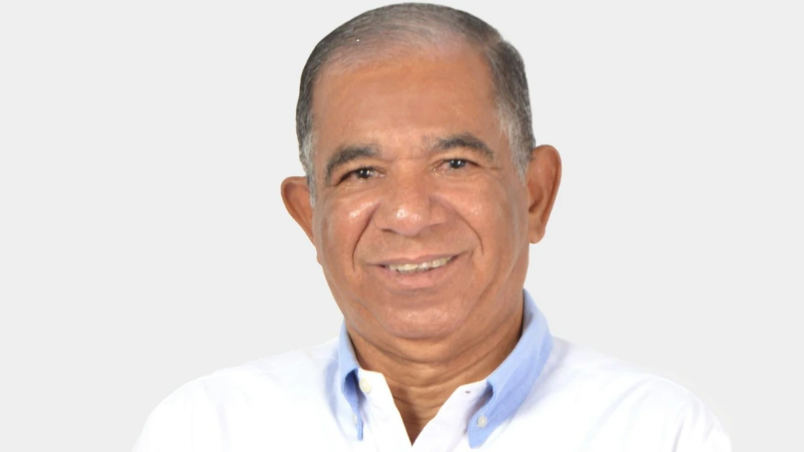 Smiling middle-aged man with short gray hair wearing a light blue collared shirt against a light gray background.