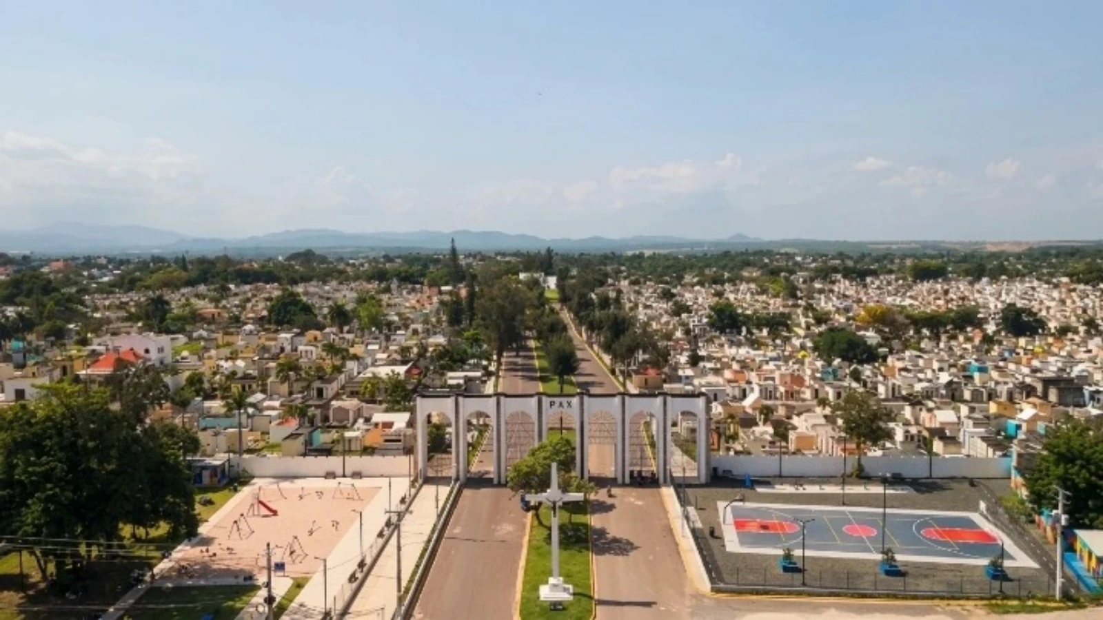Aerial view of a cemetery with a central road, a grand arch entrance labeled 'PAX', and a cross monument in front.
