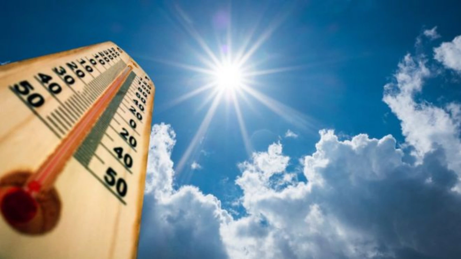 Wooden thermometer tilted toward a blazing sun in a clear blue sky with white clouds, conveying hot summer weather.