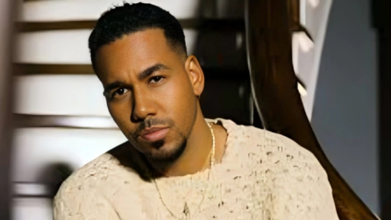 Portrait of a man with short black hair and a light beard, wearing a beige textured shirt, looking at the camera.