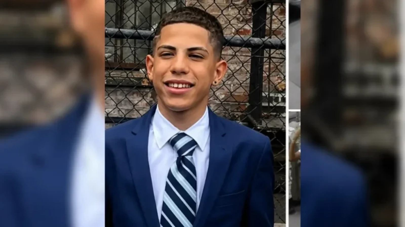 Young man in a navy blazer and striped tie smiles at the camera with a chain-link fence behind him.