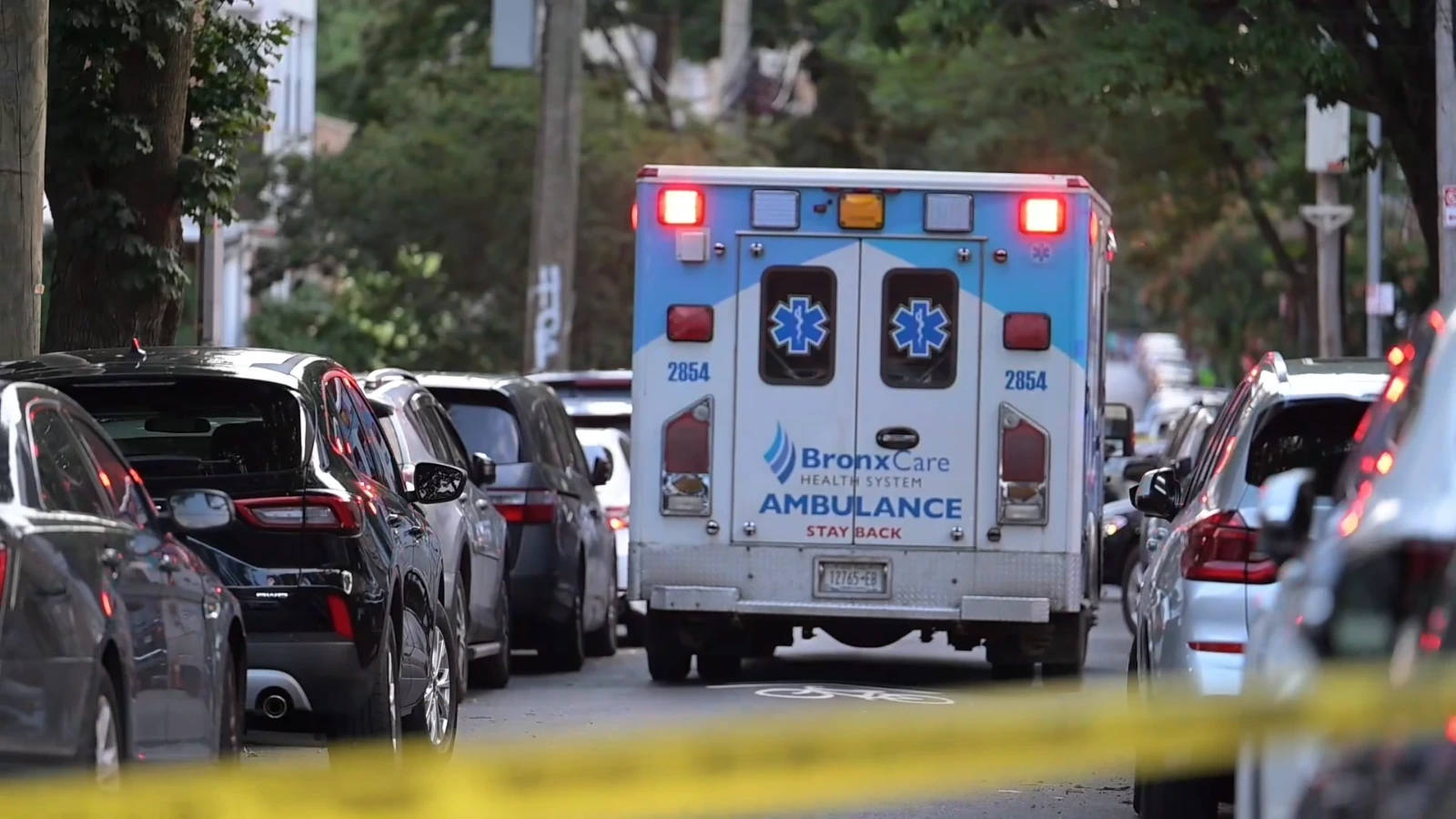 Ambulance driving down a city street with yellow caution tape in the foreground.