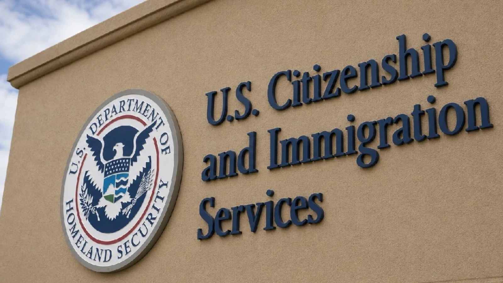 Exterior USCIS sign on a beige wall, with the Department of Homeland Security seal nearby